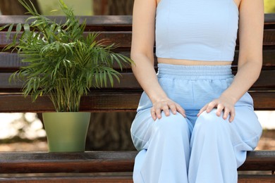 Photo of Woman with potted chamaedorea palm on bench outdoors, closeup