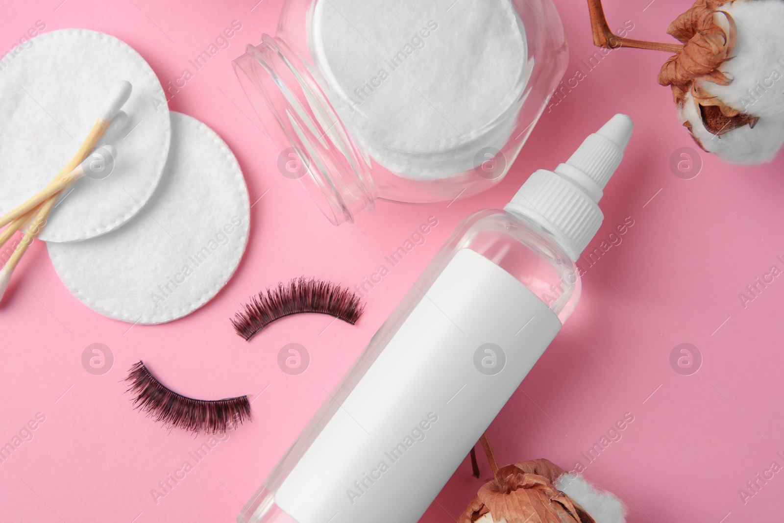 Photo of Bottle of makeup remover, cotton flowers, pads, swabs and false eyelashes on pink background, flat lay