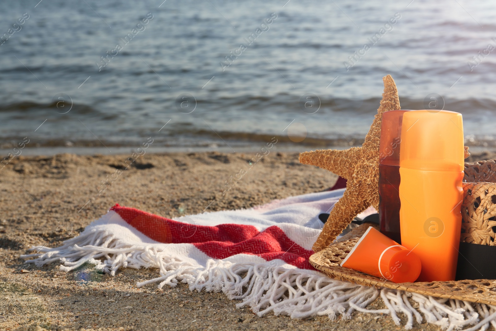 Photo of Sun protection products, hat and starfish on blanket near sea, space for text