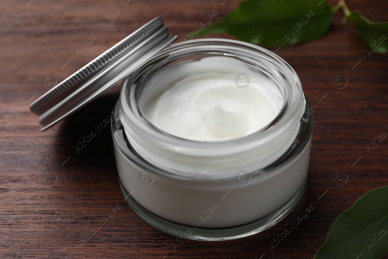 Photo of Jar of face cream and green leaves on wooden table, closeup