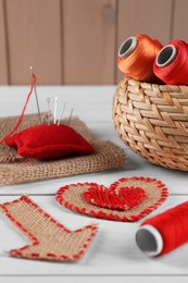 Photo of Pieces of burlap fabric, spools of threads, pincushion and needles on white wooden table