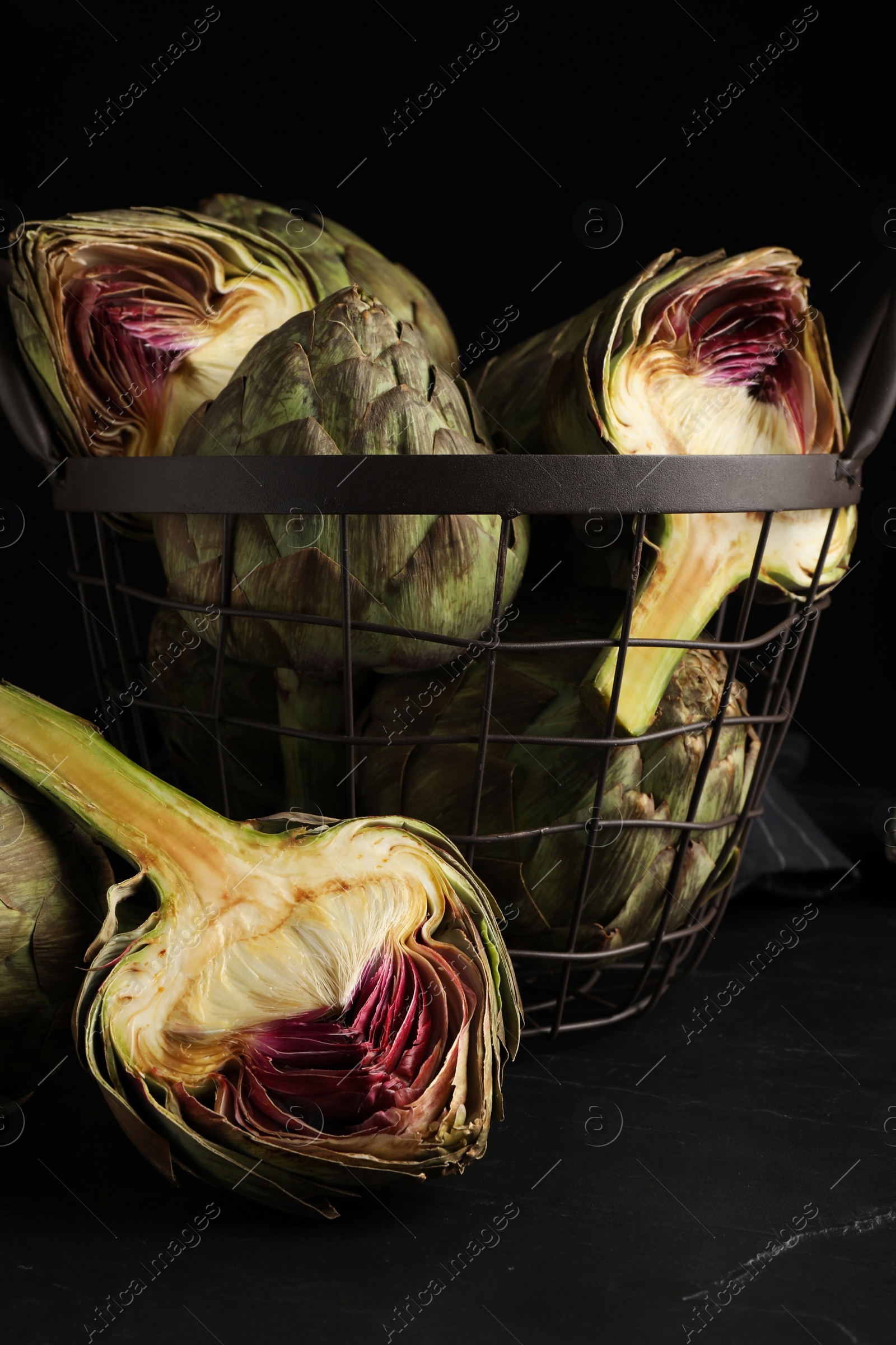 Photo of Cut and whole fresh raw artichokes on black table