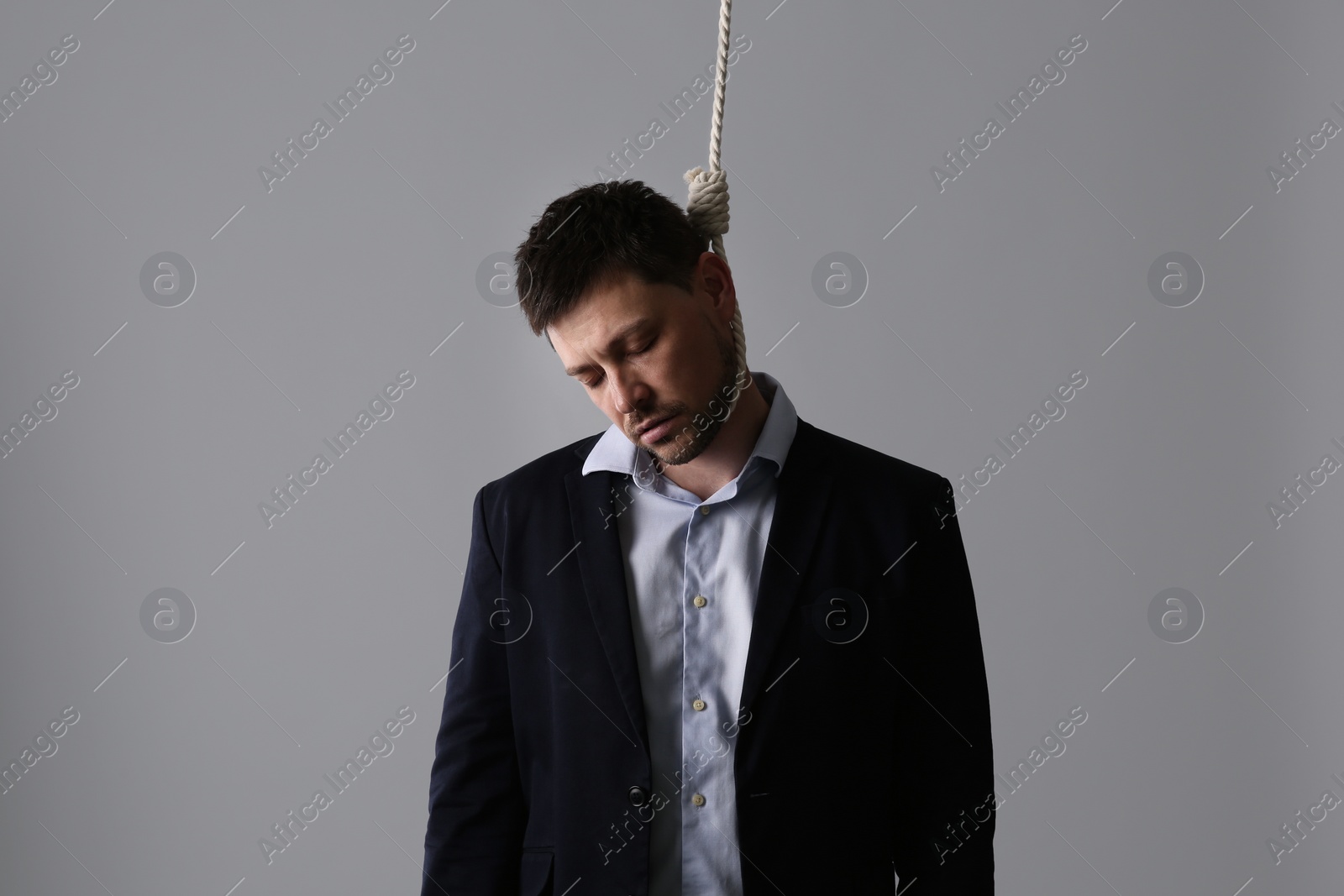 Photo of Depressed businessman with rope noose on neck against light grey background