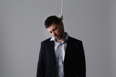 Photo of Depressed businessman with rope noose on neck against light grey background