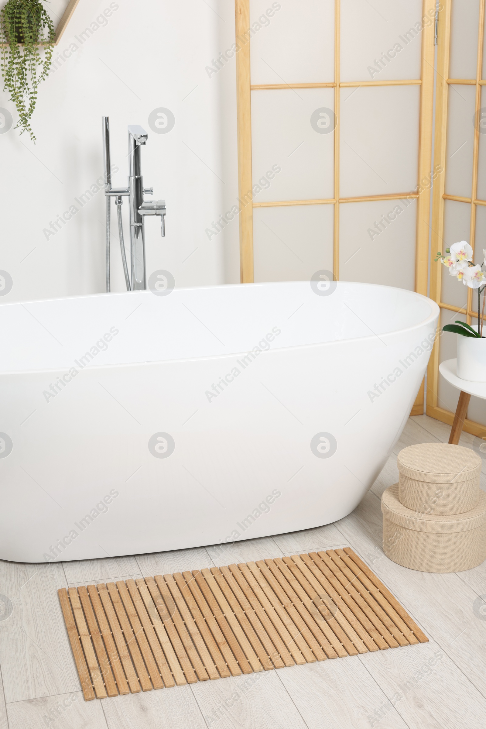 Photo of Stylish bathroom interior with bath tub, houseplants and bamboo mat