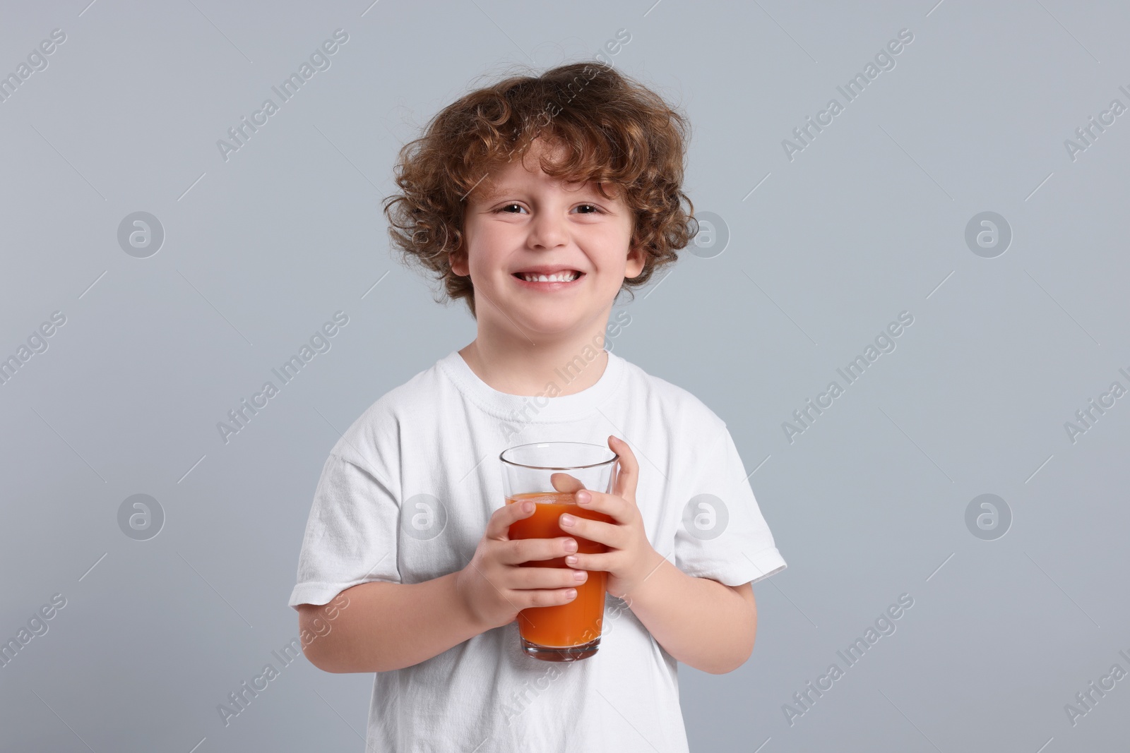 Photo of Cute little boy with glass of fresh juice on light gray background