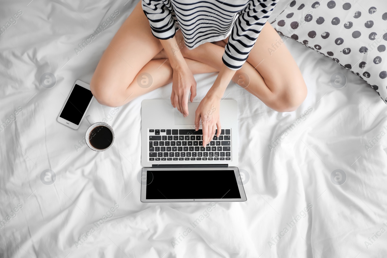 Photo of Female blogger with laptop and cup of coffee on bed, top view