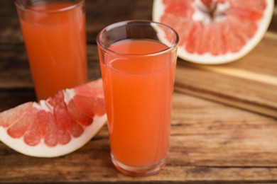 Photo of Glass of pink pomelo juice and fruit on wooden table, closeup
