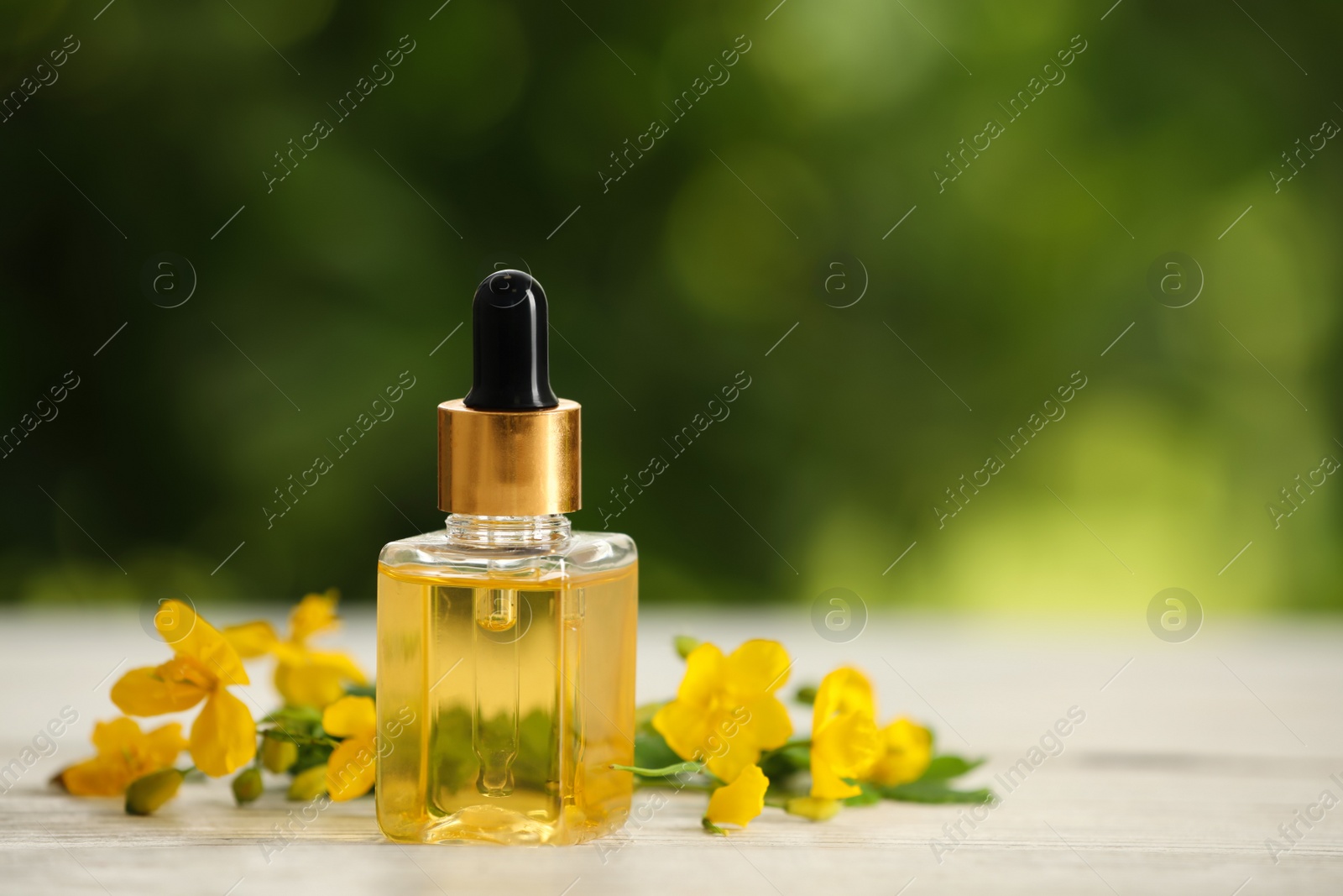 Photo of Bottle of natural celandine oil near flowers on white wooden table outdoors, space for text