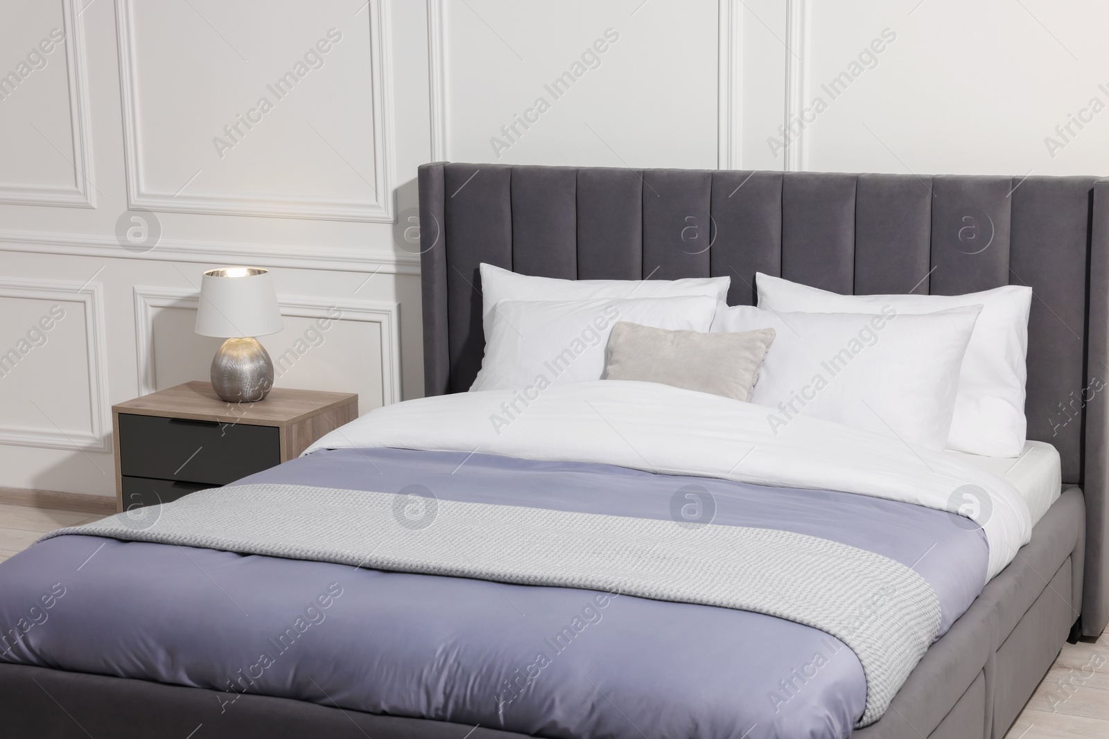 Photo of Comfortable bed near bedside table with lamp at home. Interior design