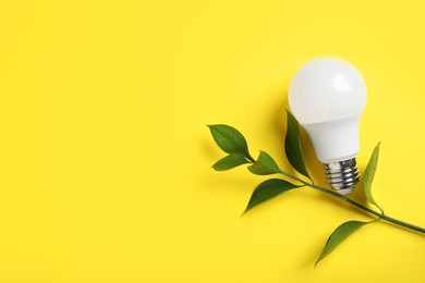 Photo of Light bulb and branch with green leaves on yellow background, flat lay. Space for text