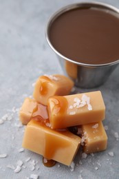 Yummy caramel candies, sauce and sea salt on grey table, closeup