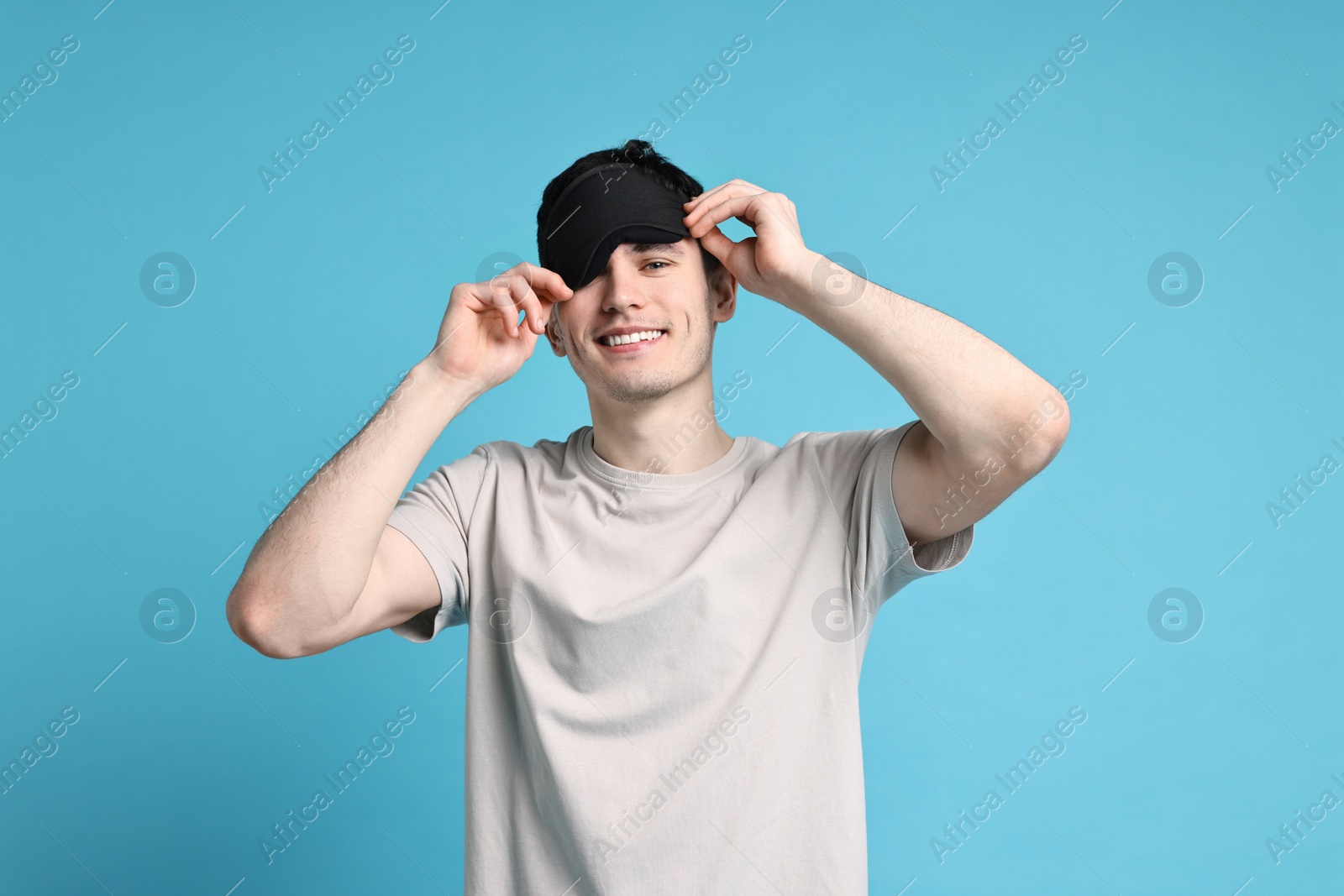 Photo of Happy man in pyjama and sleep mask on light blue background