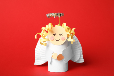 Photo of Toy angel made of toilet paper hub on red background
