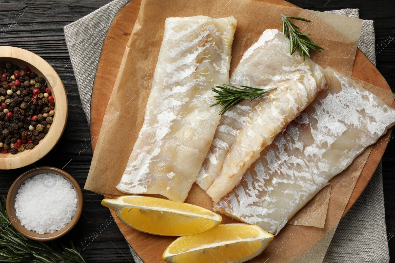 Photo of Fresh raw cod fillets, spices and lemon on wooden table, flat lay