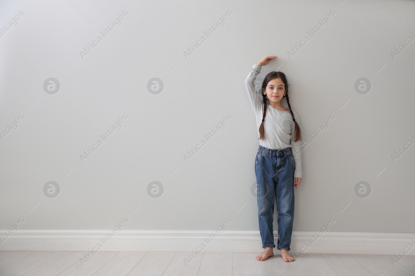 Photo of Little girl measuring her height near light grey wall indoors. Space for text