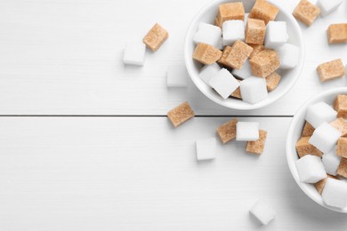 Different sugar cubes in bowls on white wooden table, flat lay. Space for text