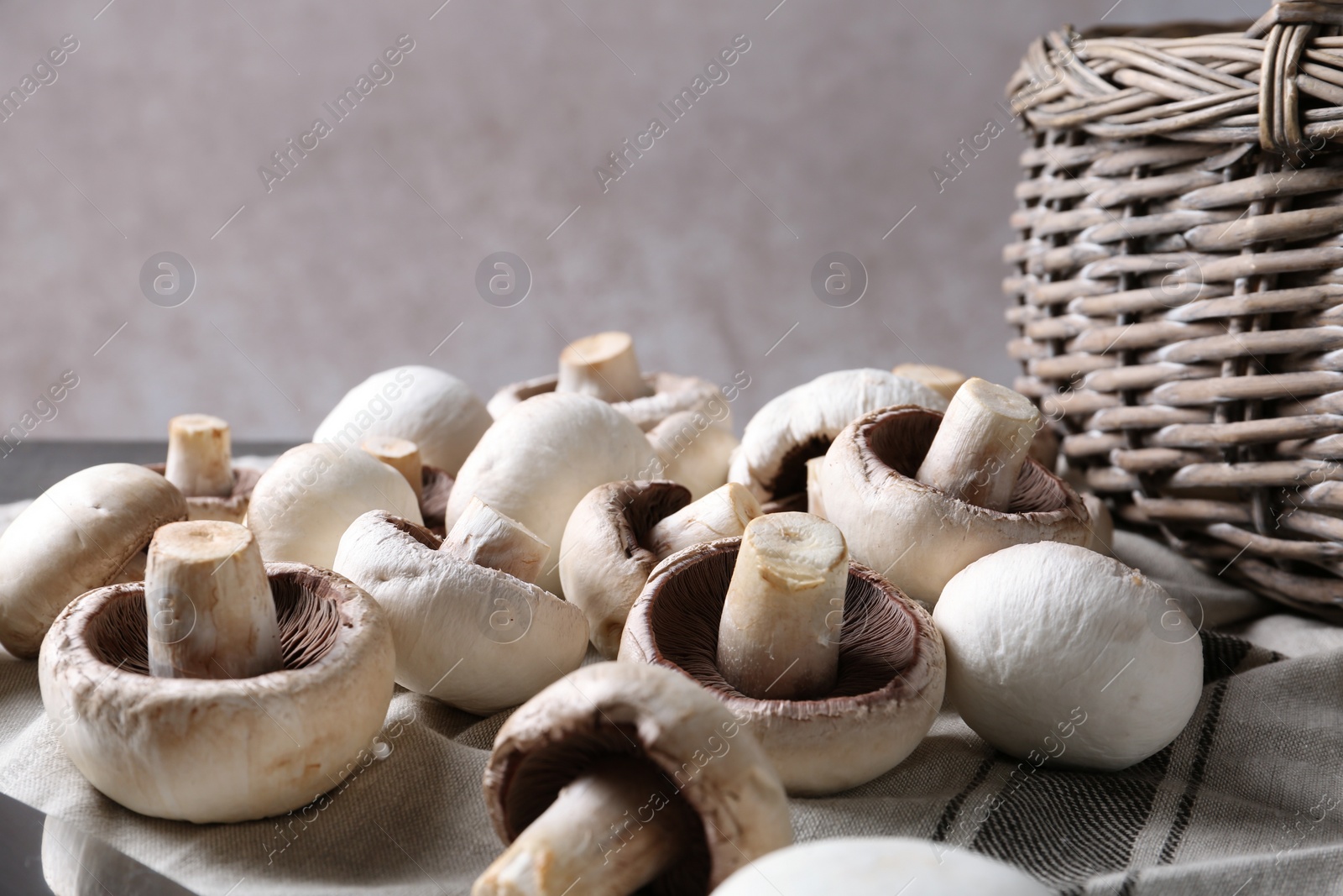 Photo of Fresh champignon mushrooms and basket on fabric, closeup. Space for text