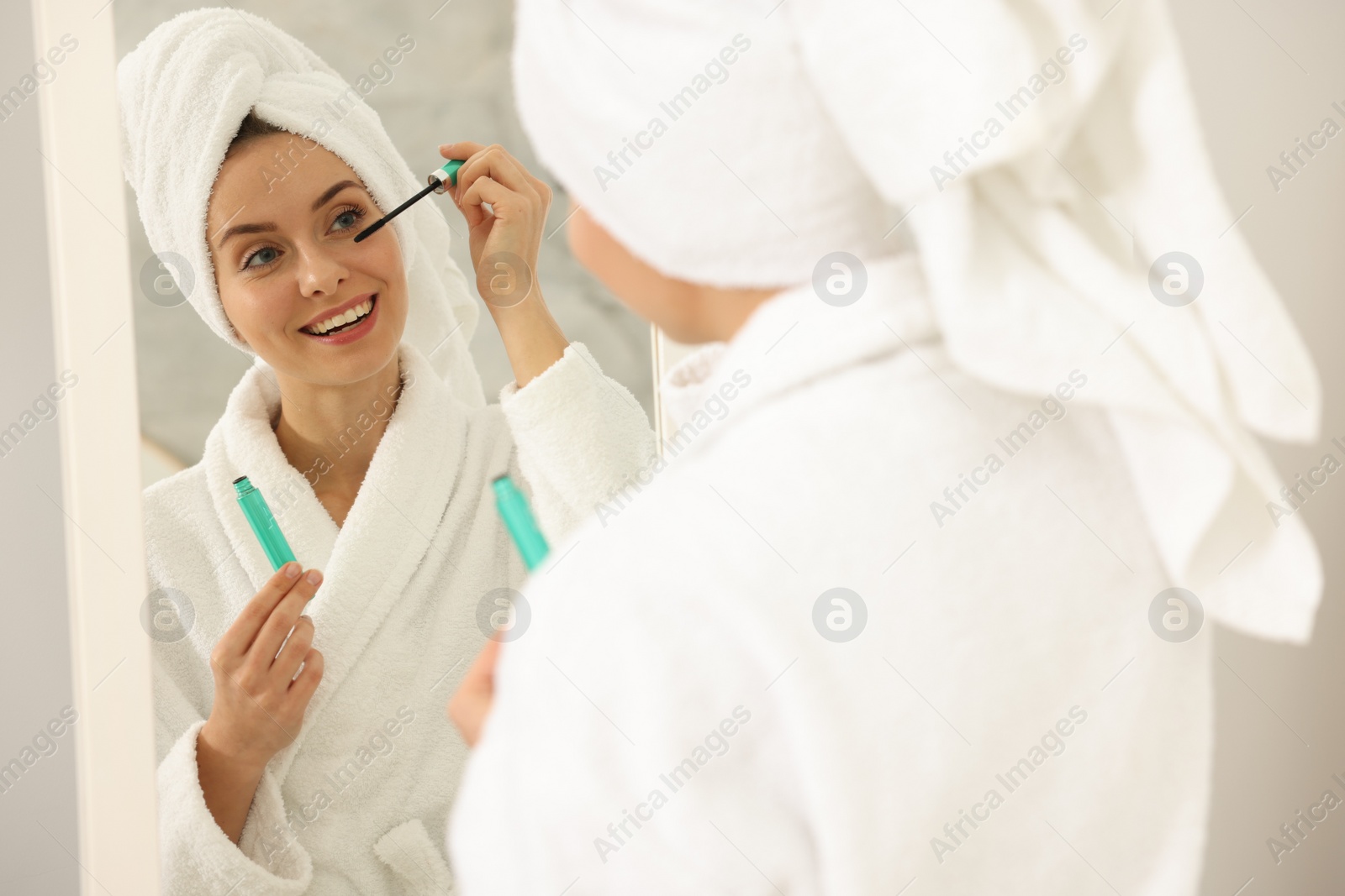 Photo of Beautiful woman applying mascara near mirror in bathroom