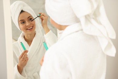 Beautiful woman applying mascara near mirror in bathroom