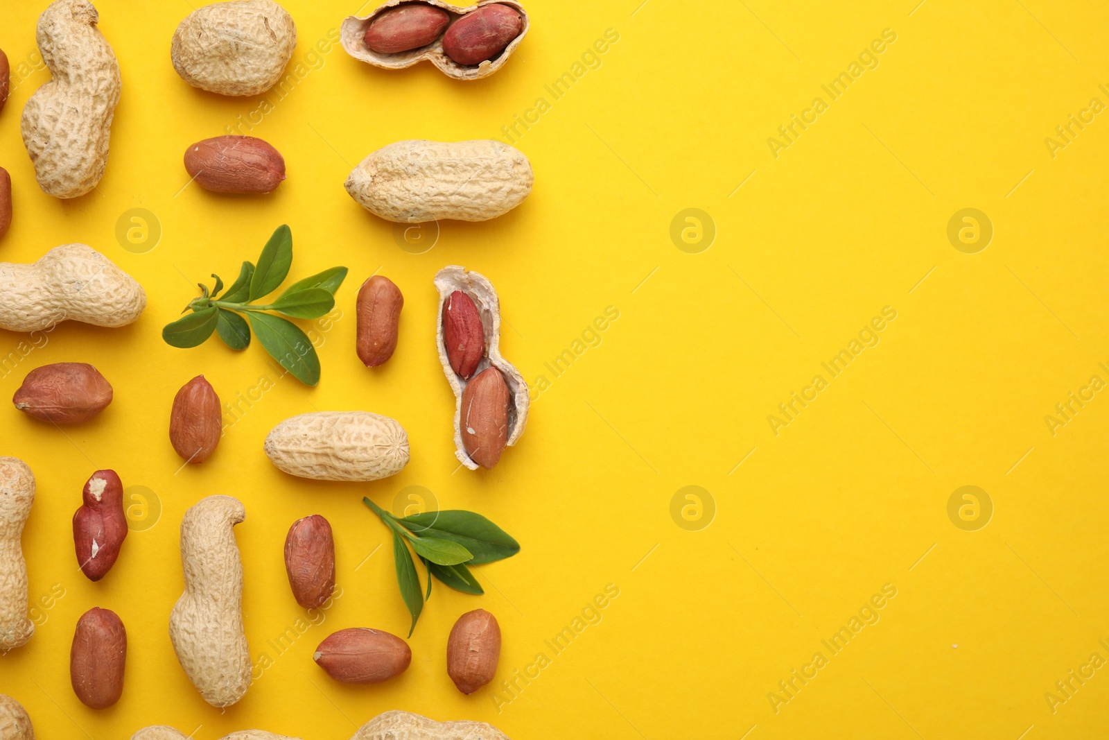 Photo of Fresh peanuts and leaves on yellow table, flat lay. Space for text