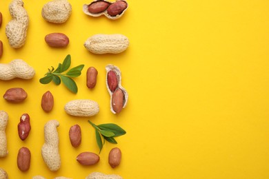 Fresh peanuts and leaves on yellow table, flat lay. Space for text