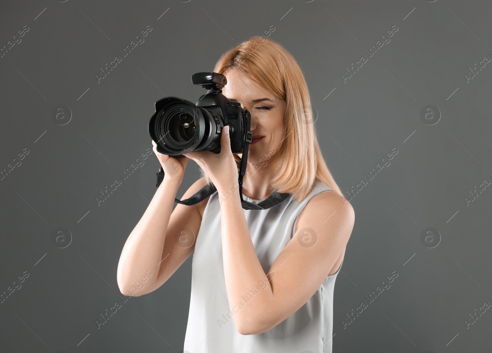 Photo of Young woman with camera against gray background. Professional photo studio