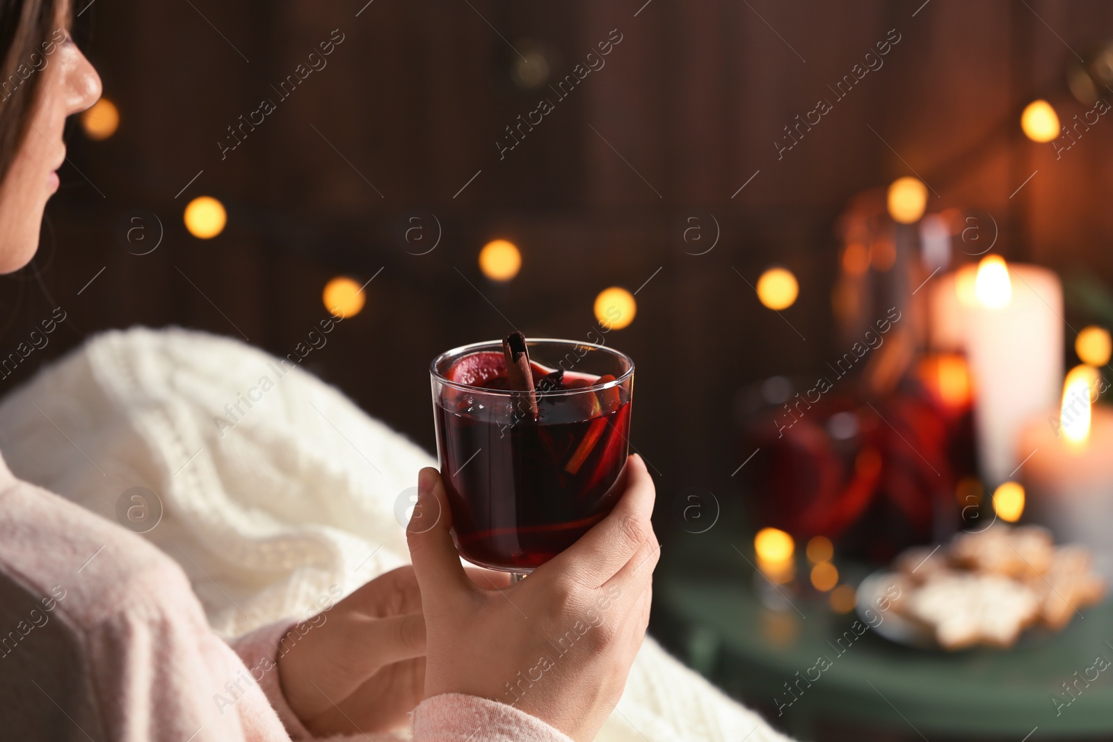 Photo of Woman with glass of mulled wine at home, focus on hands. Space for text