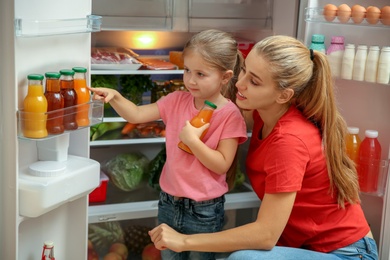 Photo of Young mother and daughter choosing juice in refrigerator at home