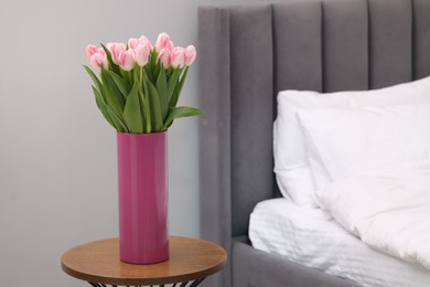 Beautiful bouquet of fresh pink tulips on bedside table in bedroom