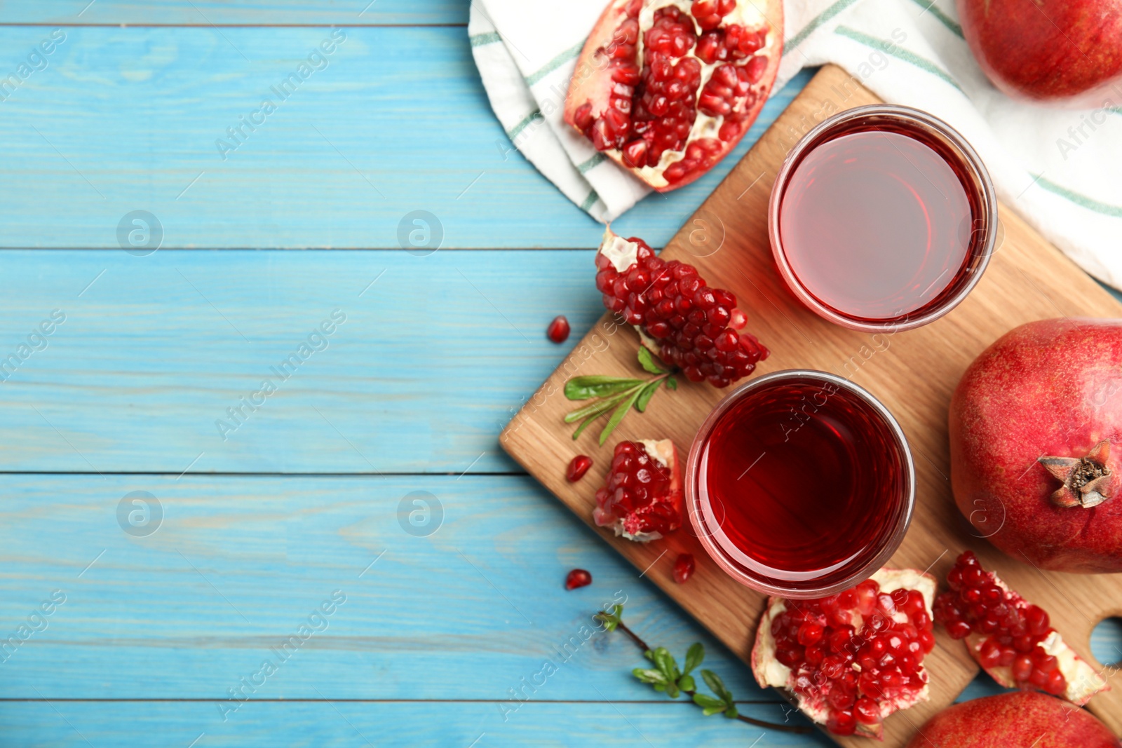 Photo of Glasses of pomegranate juice and fresh fruits on light blue wooden table, flat lay. Space for text