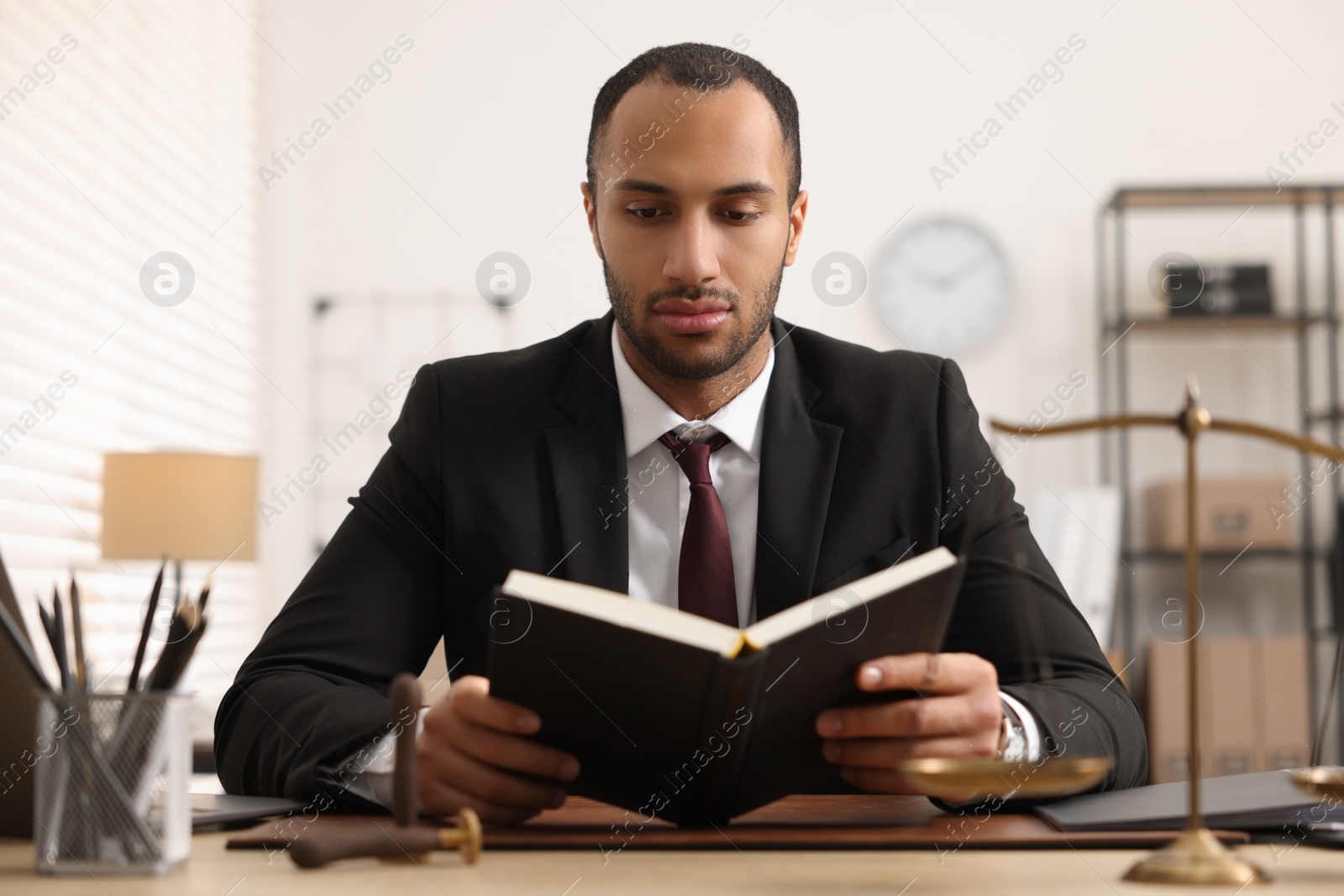 Photo of Serious lawyer reading book at table in office