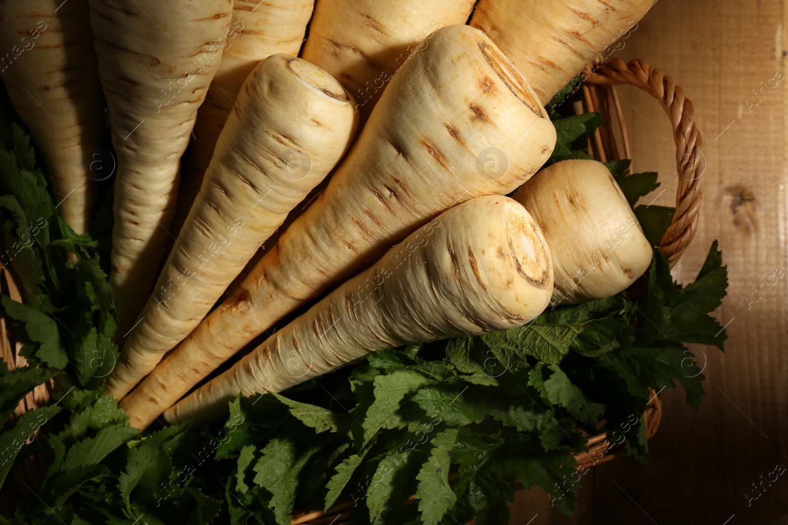 Photo of Wicker basket with delicious fresh ripe parsnips and green leaves on wooden table, top view