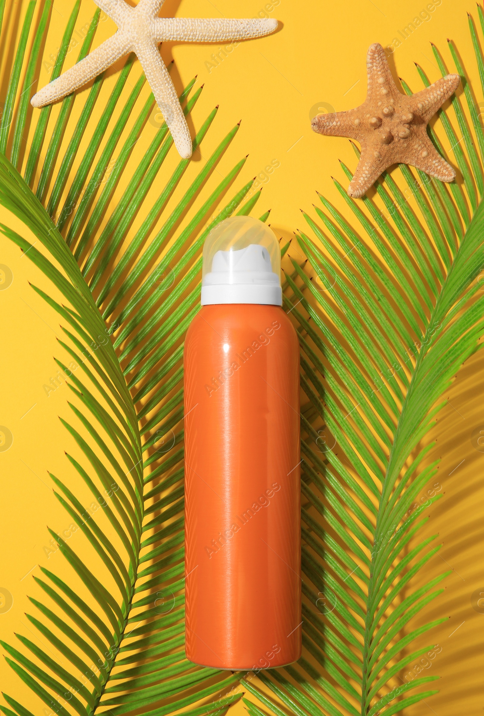 Photo of Sunscreen, sea stars and tropical leaves on yellow background, flat lay. Sun protection care