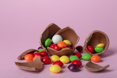 Photo of Broken chocolate egg with colorful candies on pink background