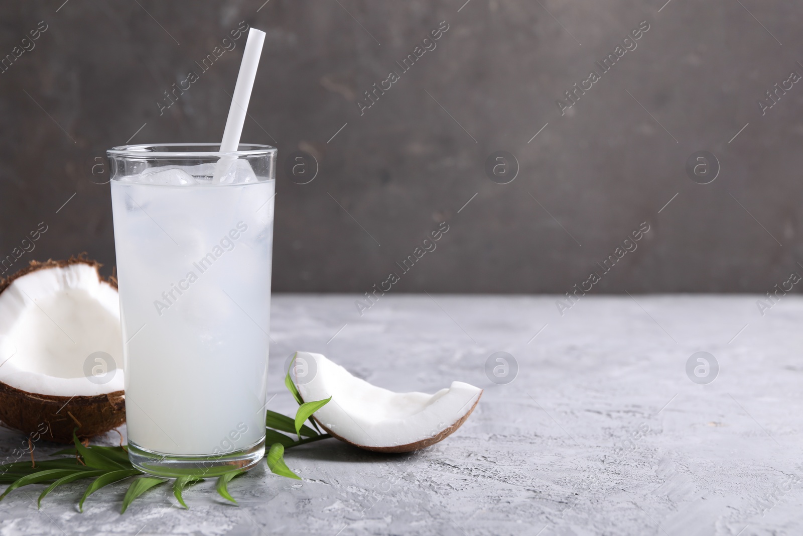 Photo of Glass of coconut water with ice cubes, palm leaf and nut on grey table. Space for text