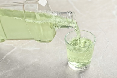 Pouring mouthwash in glass on light background. Teeth care