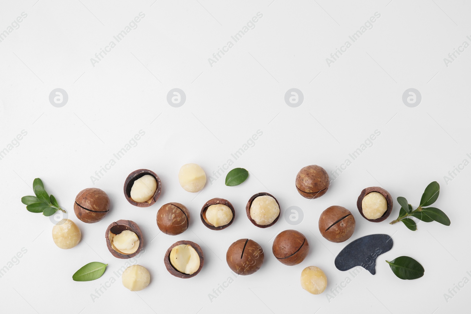 Photo of Tasty Macadamia nuts and green leaves on white background, flat lay. Space for text