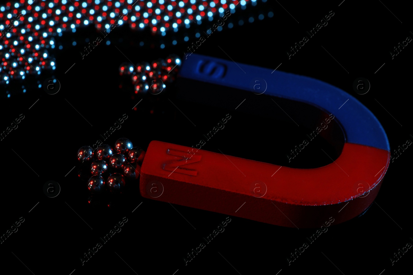 Photo of Magnet attracting chrome balls on black background. Business leadership concept