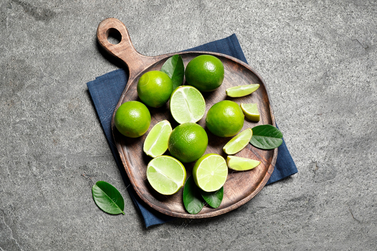 Photo of Fresh ripe limes and leaves on grey table, top view