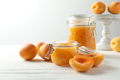 Photo of Jars of apricot jam and fresh fruits on white wooden table