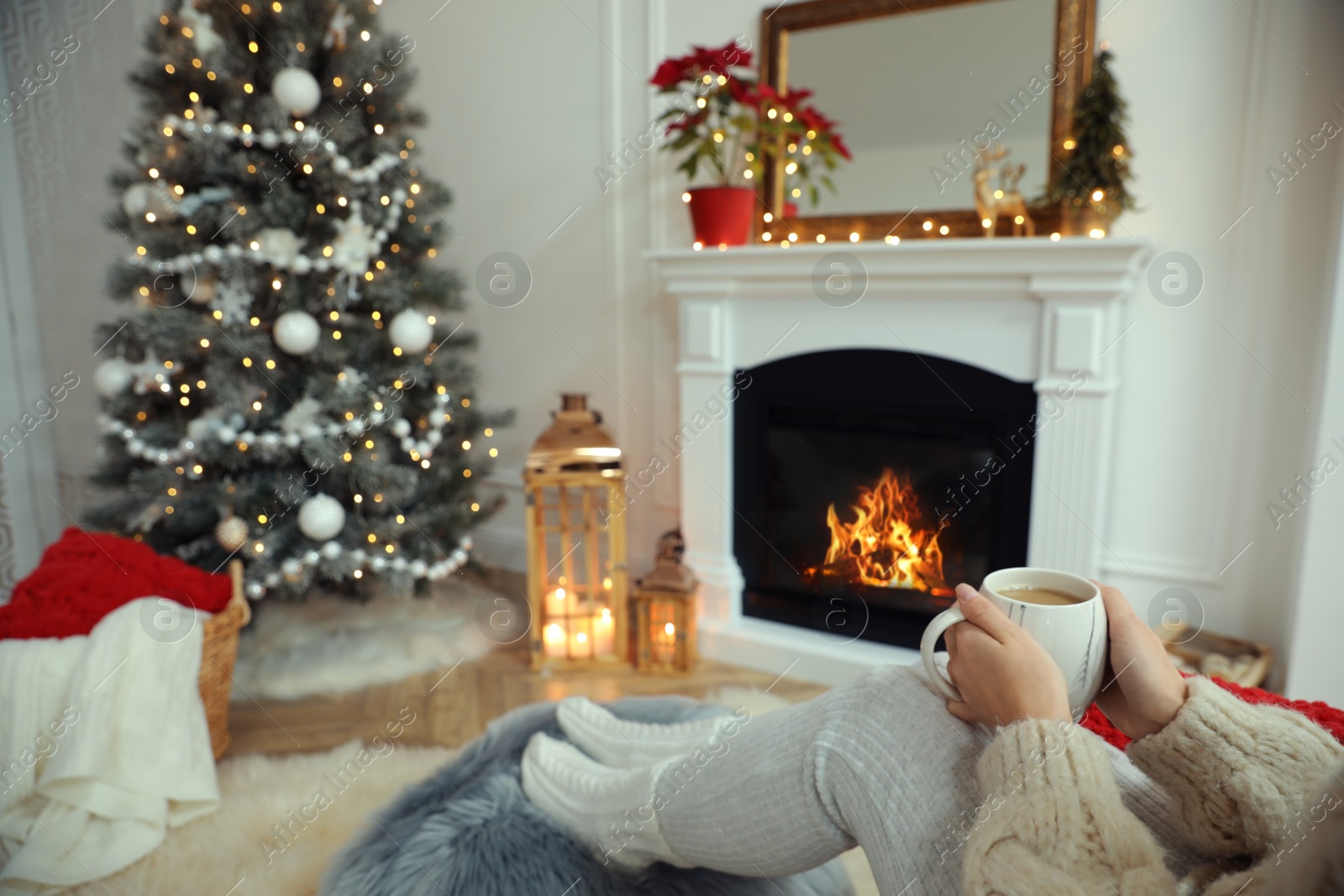 Photo of Woman with hot drink resting near fireplace in cozy room decorated for Christmas, closeup