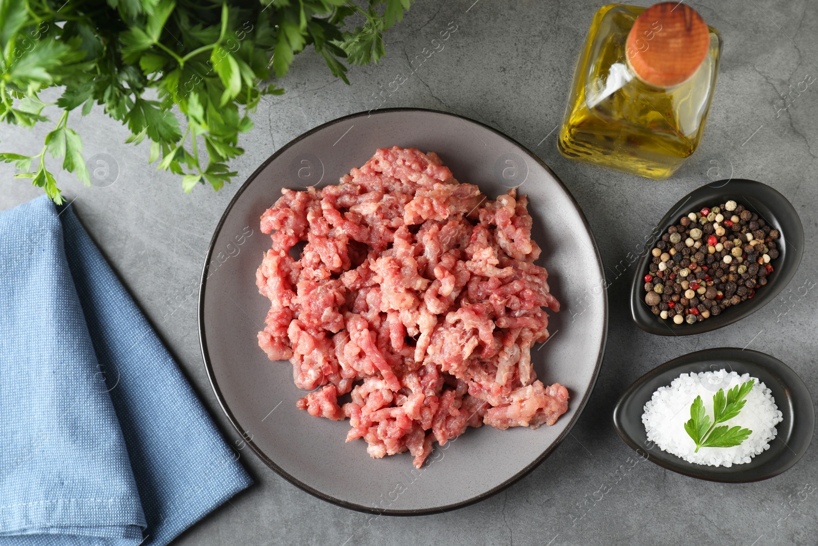 Photo of Raw ground meat, spices, parsley and oil on grey table, flat lay