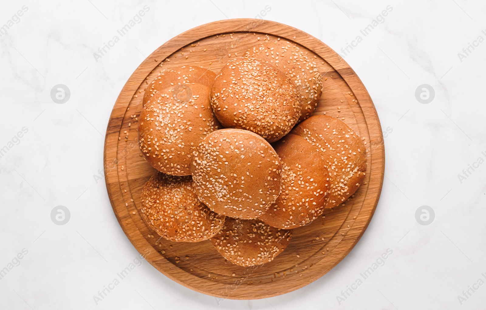 Photo of Fresh buns with sesame seeds on white marble table, top view