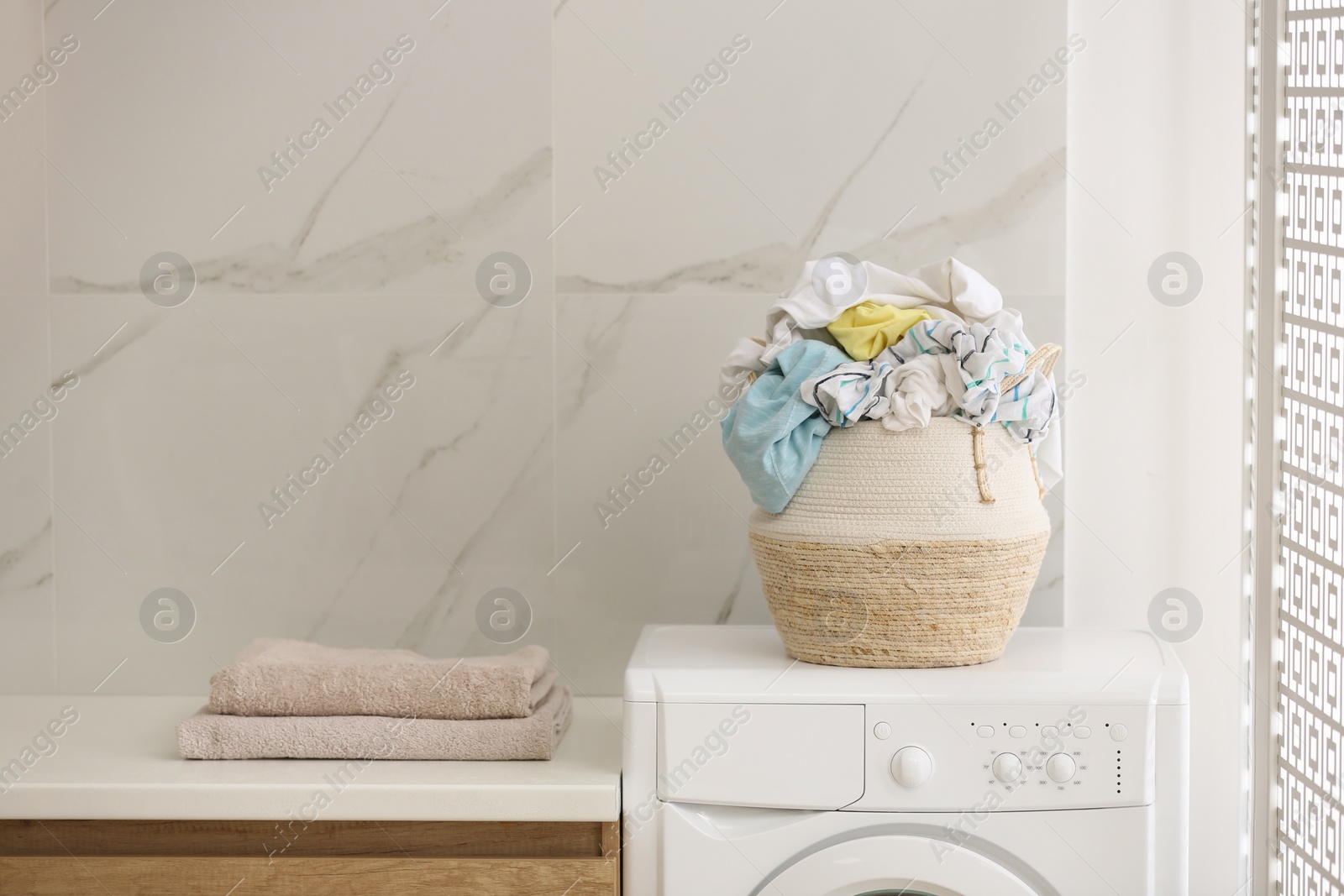 Photo of Wicker basket with dirty clothes on washing machine in bathroom. Space for text