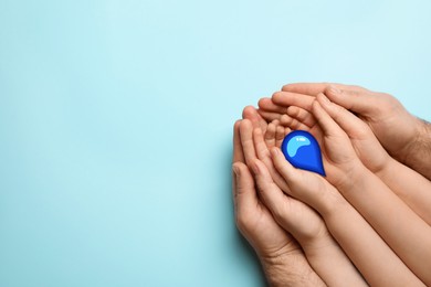 Image of Family holding paper water drop on light blue background, top view. Space for text