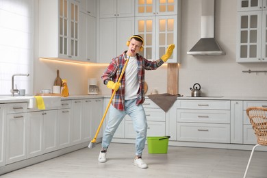 Photo of Handsome young man with headphones singing while cleaning kitchen