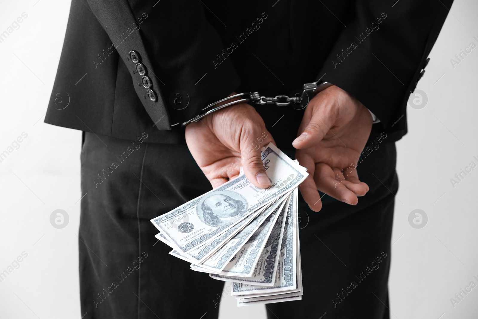 Photo of Man in handcuffs holding bribe money on light background, closeup
