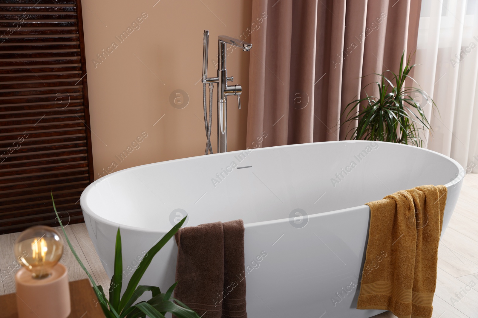 Photo of Stylish bathroom interior with ceramic tub, terry towels and houseplants