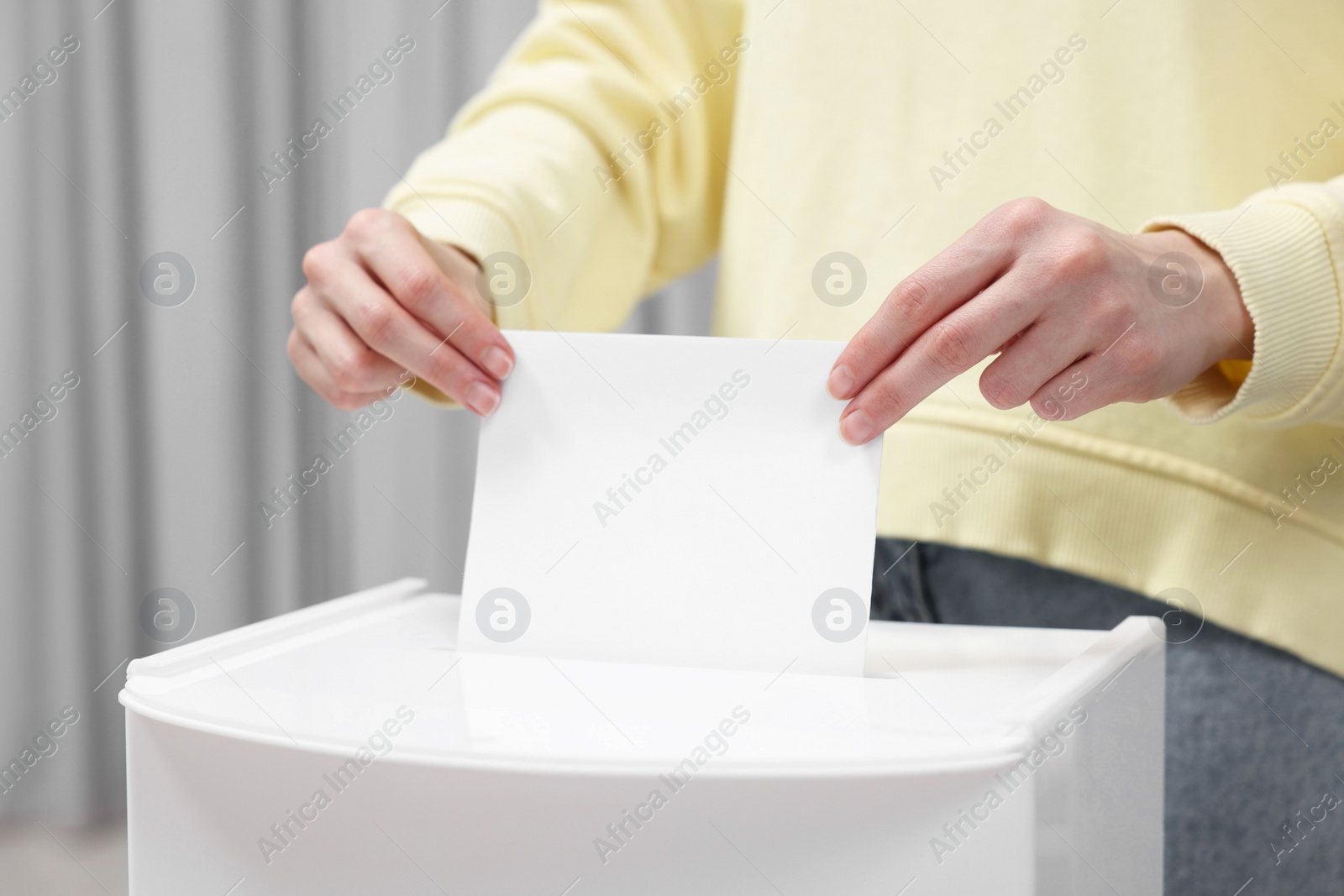 Photo of Woman putting her vote into ballot box on blurred background, closeup